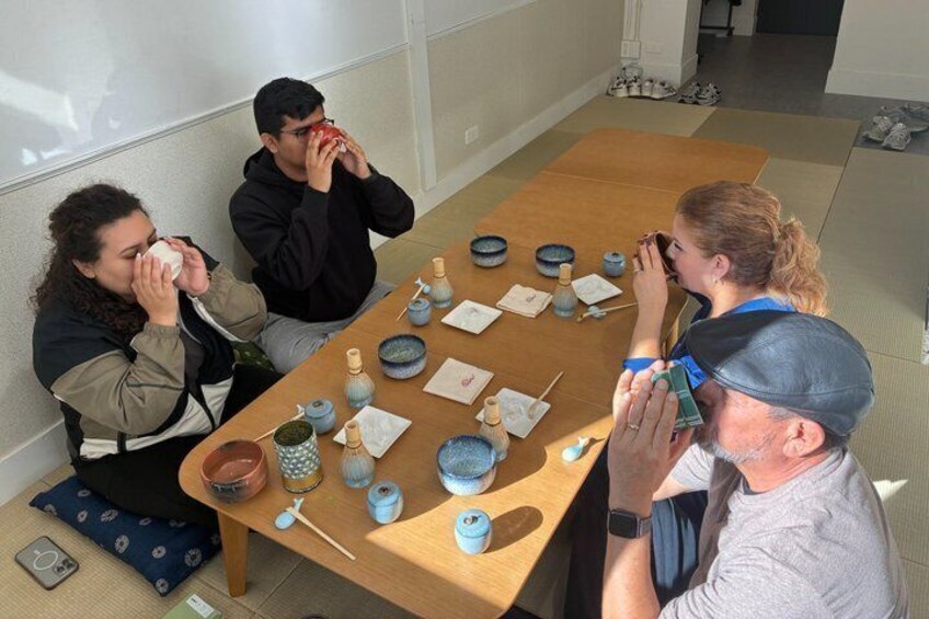 Four people sitting around a table with bowls and chopsticks, likely engaged in a meal or tea ceremony. 1