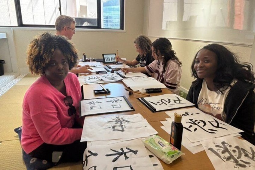 A group of people seated at a table with papers and writing instruments, engaged in an activity that involves writing or drawing on the papers. 5