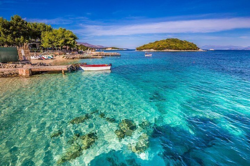 A coastal scene with clear turquoise waters, a small boat docked at a pier, and a distant island. 3
