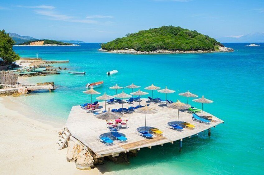 A wooden pier with beach chairs and umbrellas, a sandy beach, and a small island in the background. 2