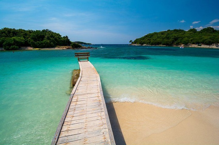 Une jetée en bois s’avance dans des eaux turquoise, menant à une plage de sable fin, avec une végétation luxuriante en arrière-plan. 2