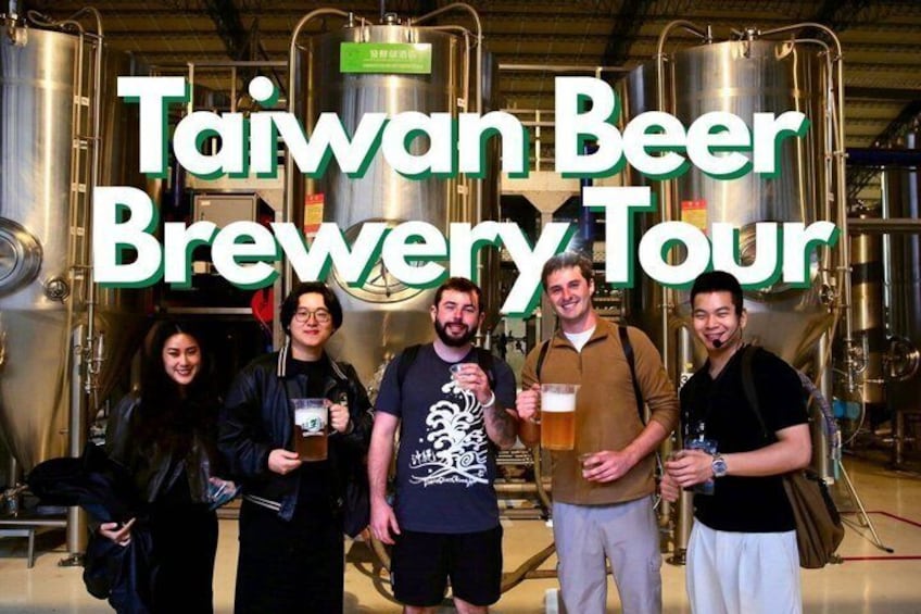 A group of people in a brewery with large brewing tanks in the background. 1