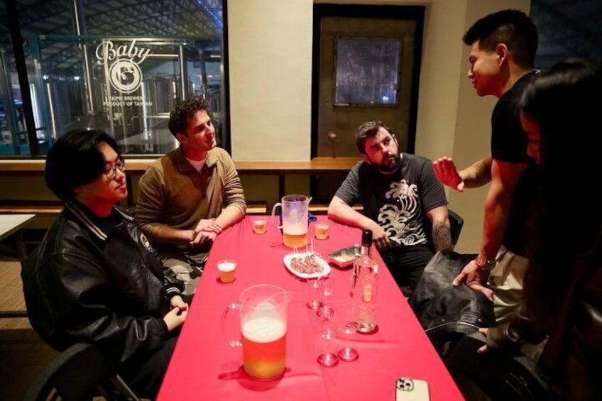 A group of people seated around a table with drinks and a pitcher, in a room with a window displaying a sign. 4