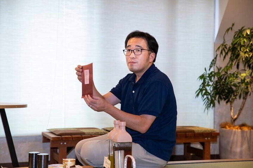 A man holding a red object in a room with a plant and a wooden table. 4