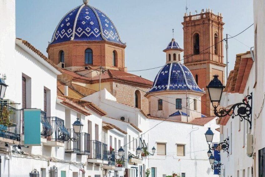 A street with white buildings, blue domes, and a red tower. 1