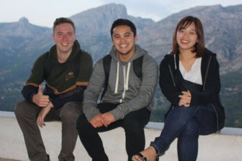 Three people sitting on a ledge with a mountainous landscape in the background. 4