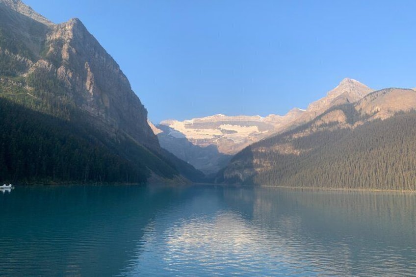 A calm lake surrounded by forested mountains under a clear sky. 2