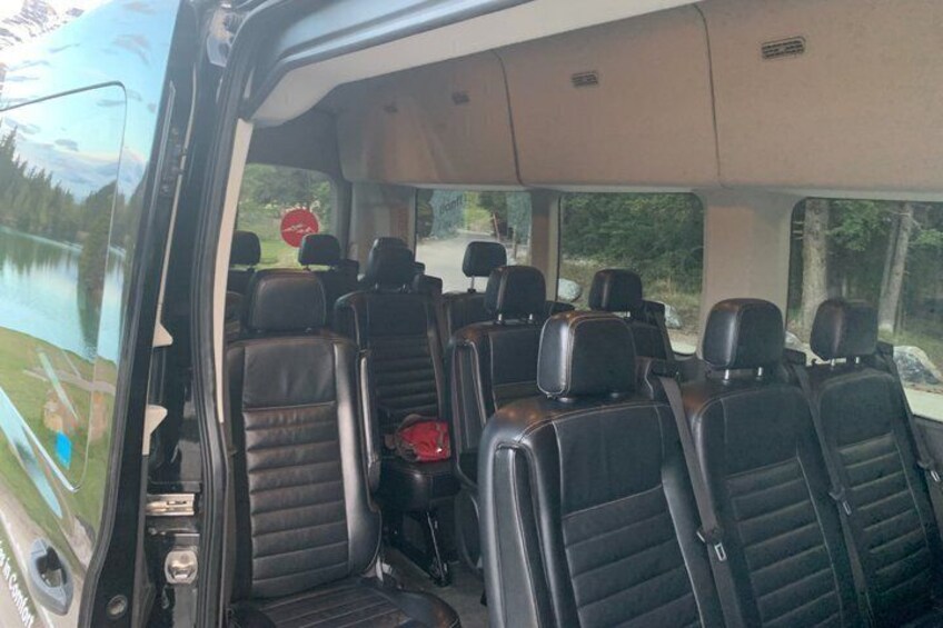 The interior of a bus with black leather seats and a central aisle. 4
