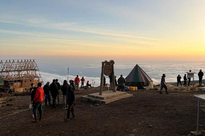 En grupp människor på en plats högt uppe i bergen, med klar himmel och en solnedgång i bakgrunden. 1