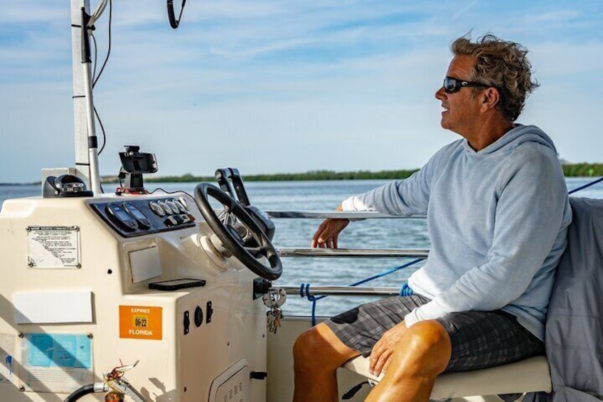A person steering a boat on a calm body of water with a clear sky and distant shoreline. 5
