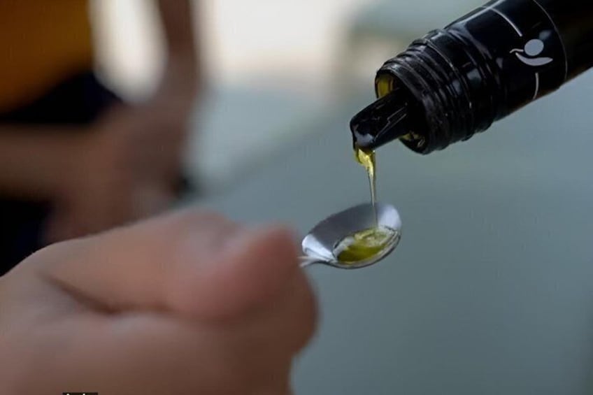 A hand holding a spoon with olive oil being poured from a bottle. 2