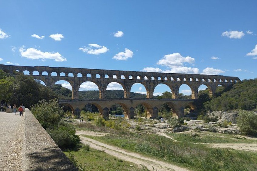 A stone aqueduct with multiple arches, a dirt path, and greenery. 2