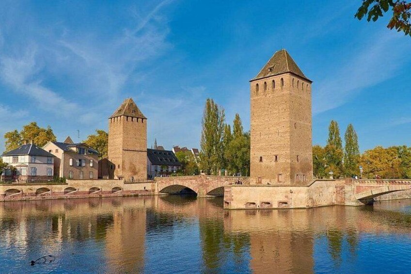 A river with two towers, a bridge, and buildings along the riverbank. 2