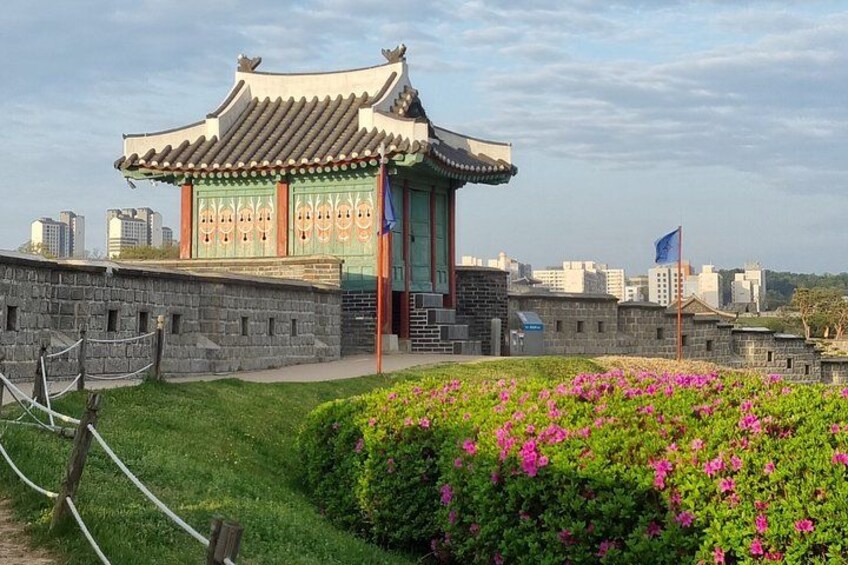 A traditional Korean building with a tiled roof, surrounded by a stone wall and a flower garden. 3