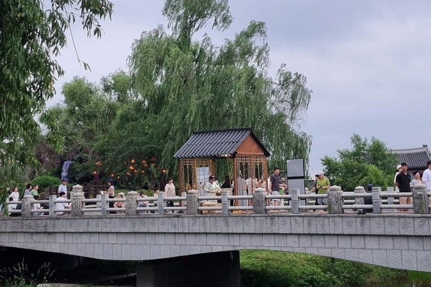 A stone bridge with a traditional pavilion, surrounded by lush greenery and trees. 5