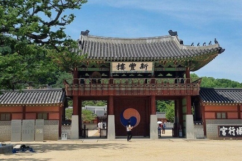 A traditional Korean gate with a blue and white emblem, surrounded by trees and a clear sky. 2