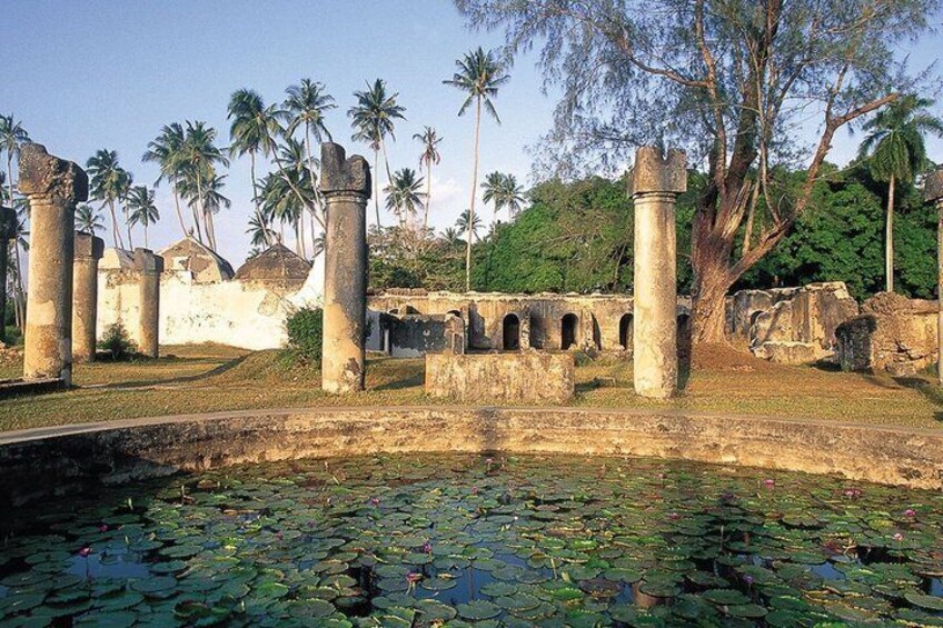 Ancient ruins with columns and arches, surrounded by palm trees and a pond with lily pads. 5
