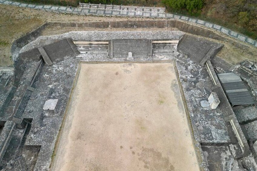 An ancient amphitheater with a central stage and tiered seating. 2