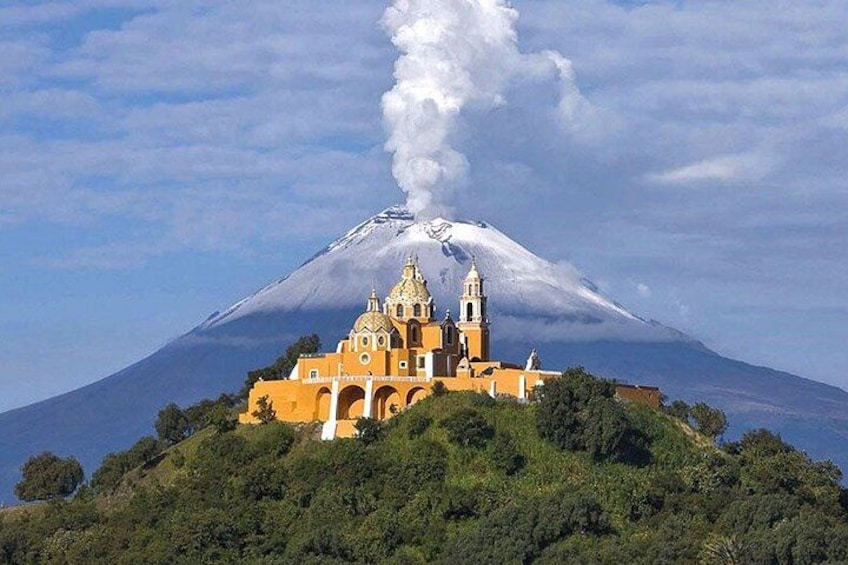 A church with a bell tower, a volcano in the background, and smoke rising from the volcano. 1