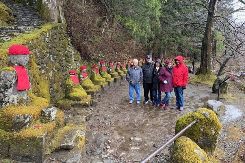 A group of people standing on a stone path with moss-covered statues and a forested background. 2