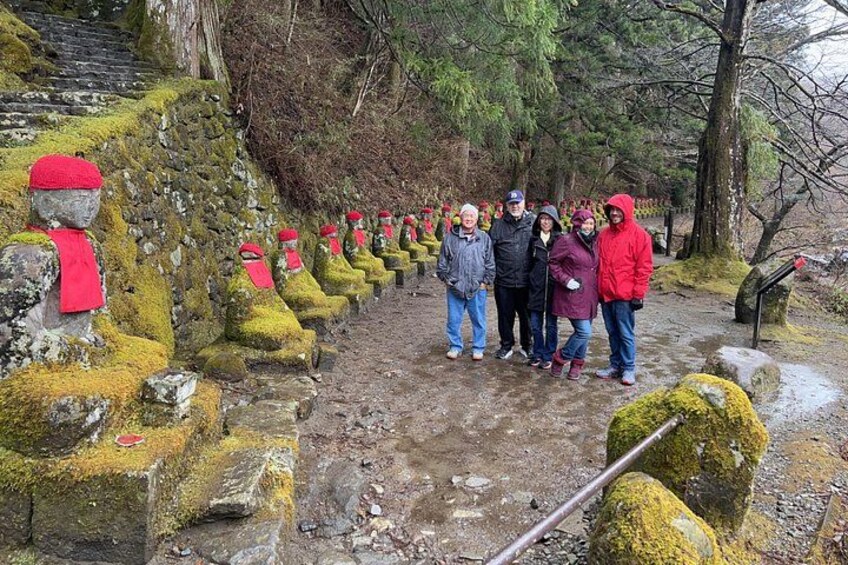 A group of people standing on a stone path with moss-covered statues, surrounded by trees and a wet ground. 5