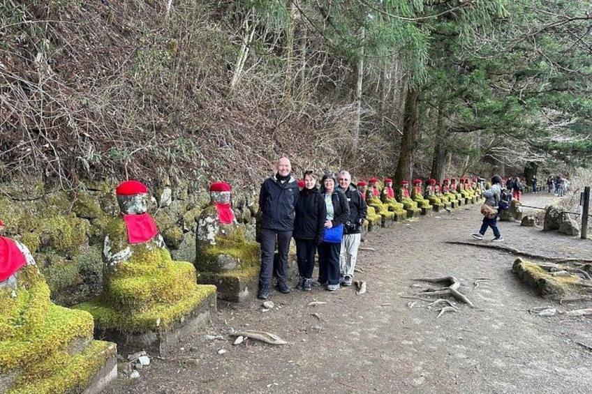 A forested area with a path lined with statues of figures wearing red hats and scarves. 4