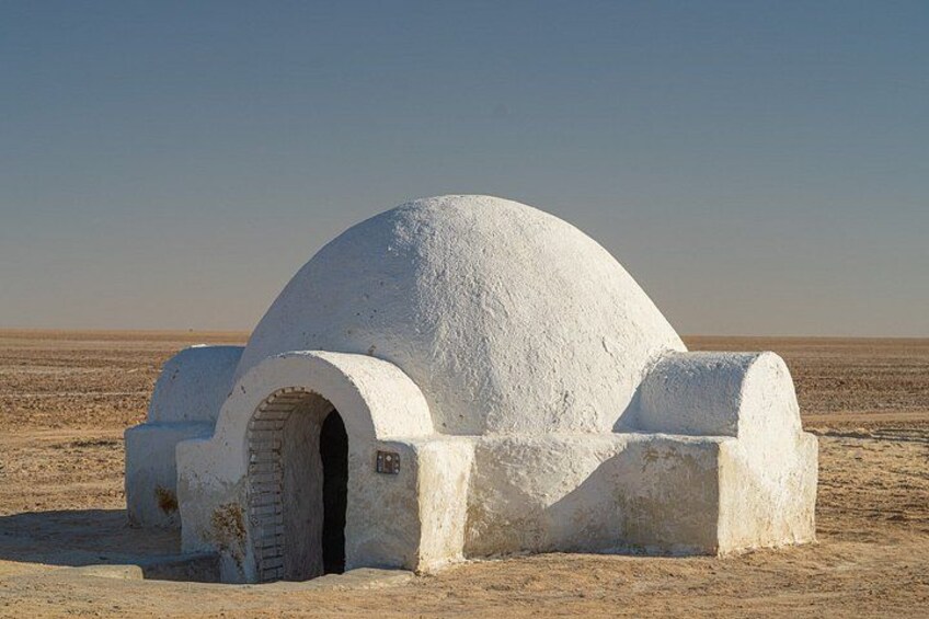 A white, dome-shaped structure with a brick entrance in a desert landscape. 4