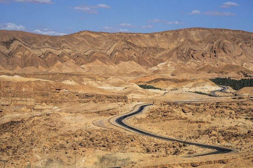 A winding road through a desert landscape with rocky terrain and distant hills. 5