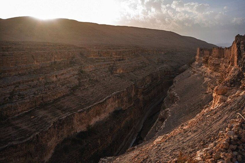 A canyon with layered rock formations and a distant sun. 1