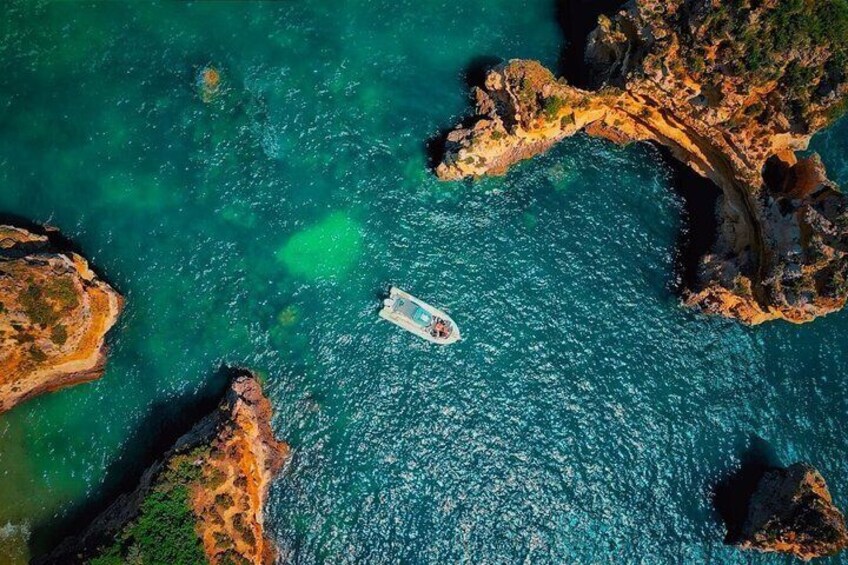 An aerial view of a boat on turquoise waters surrounded by rocky coastlines. 2