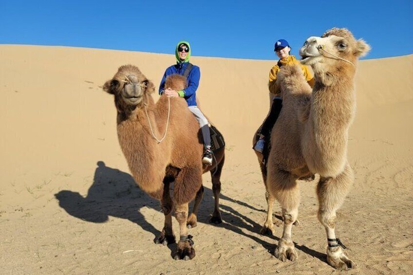 Two camels and two people riding them in a desert. 4