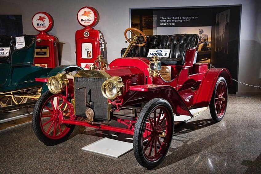 A vintage red car with a black leather interior, red wheels, and a display of red gas pumps in the background. 2
