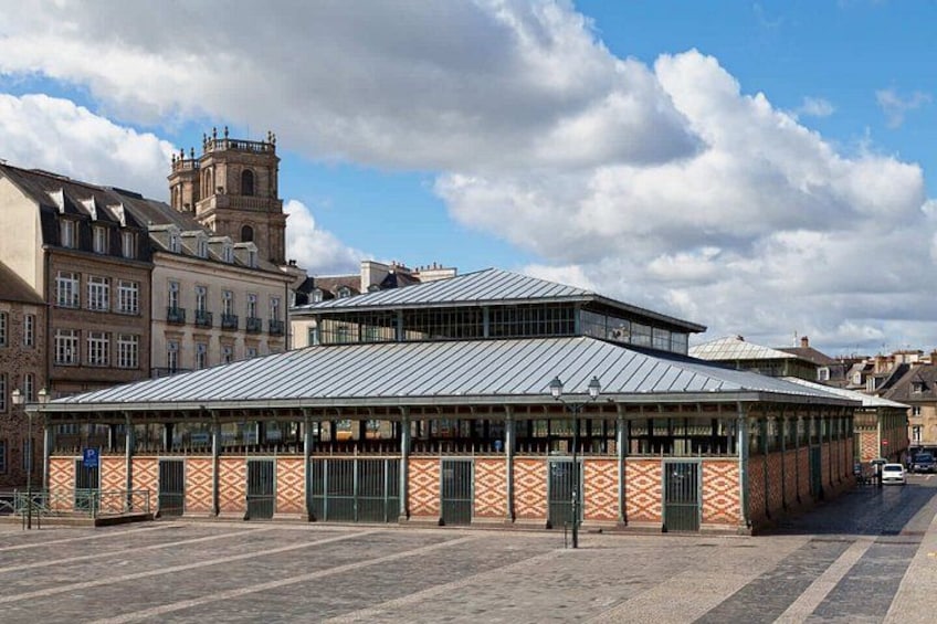 A covered public building with a patterned facade and a large open plaza in front. 2