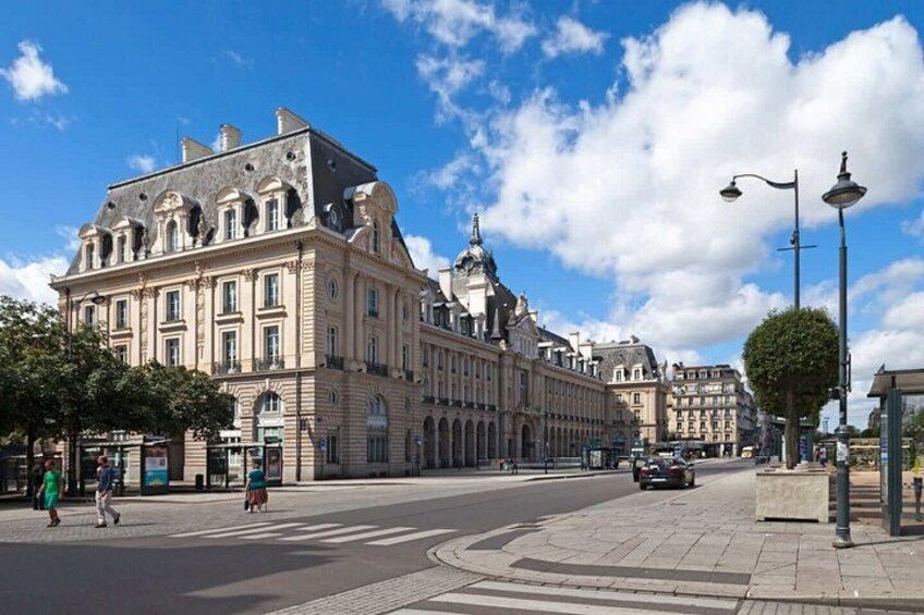 A historic building with classical architecture, a clear blue sky, and a crosswalk. 1