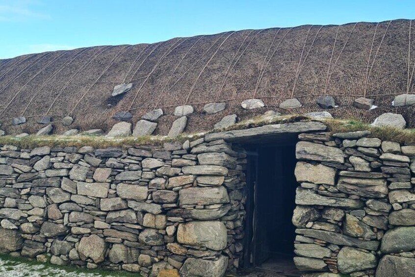 A stone structure with a doorway, surrounded by a stone wall and a large, patterned rock formation in the background. 5