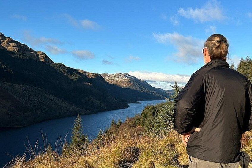 A person standing on a grassy hill overlooking a lake with mountains in the background. 3