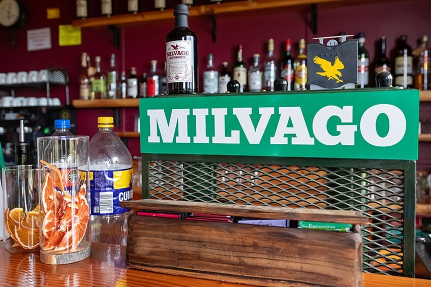A bar counter with a 'MILVAGO' sign, bottles, glasses, and dried citrus fruits. 2