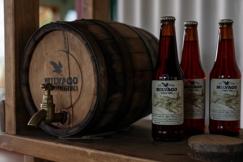 A wooden barrel with a tap and three bottles of Milvago Vermut Tonic on a wooden shelf. 1