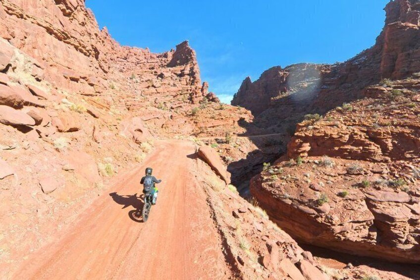 A person riding a motorcycle on a narrow, rocky trail surrounded by red rock formations. 5