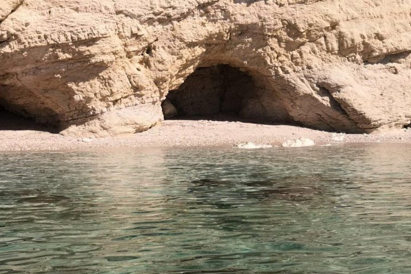 A rocky shoreline with clear water and a cave entrance. 5