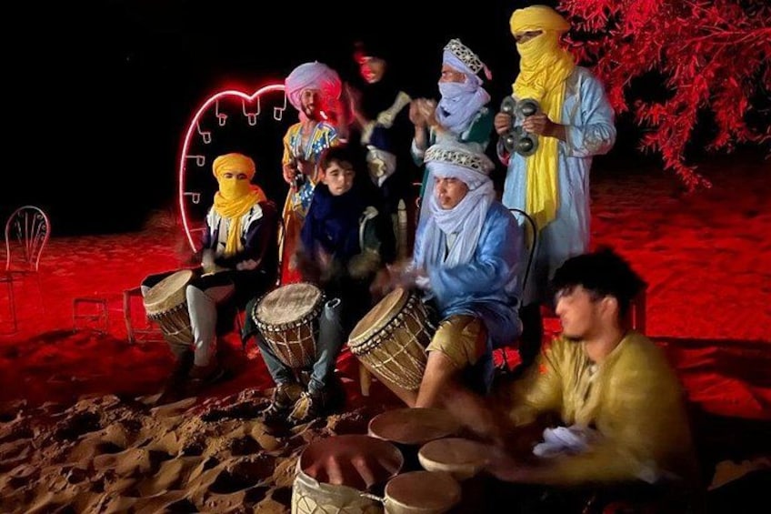 Een groep mensen speelt traditionele trommels in een woestijnlandschap bij nacht. 5