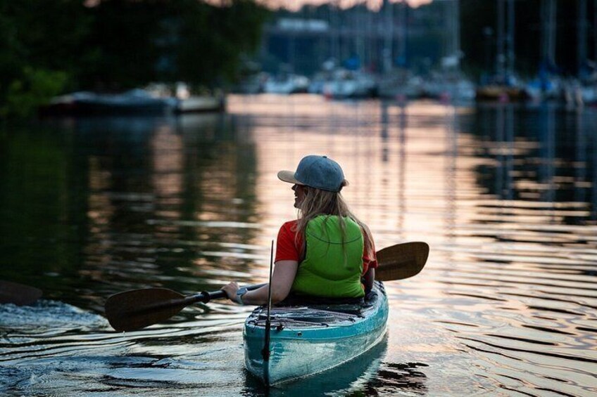 A person kayaking on a calm river with boats in the background. 2