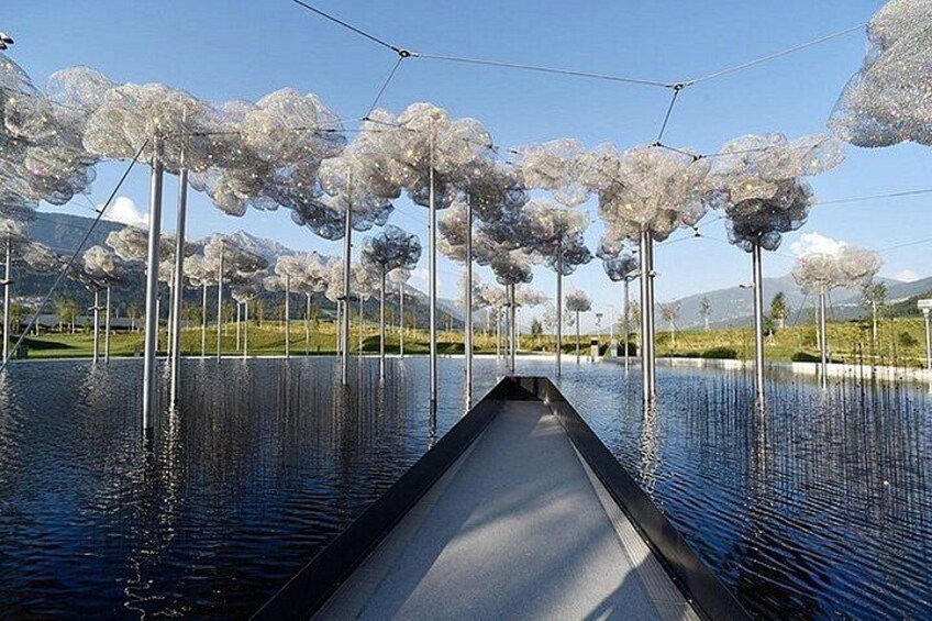 A canal with a boat, surrounded by trees with spherical tops, and a mountainous landscape in the background. 4