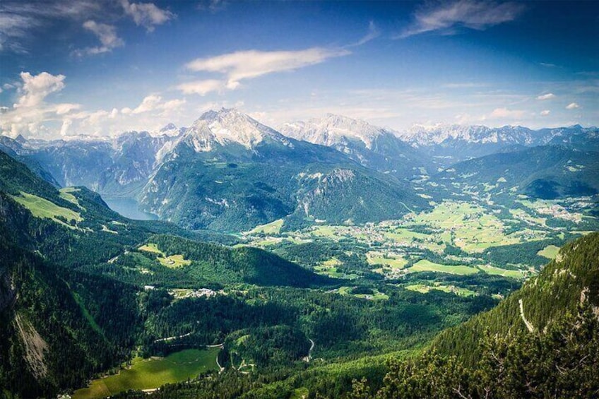 A mountainous landscape with a lake, forested valleys, and snow-capped peaks. 1