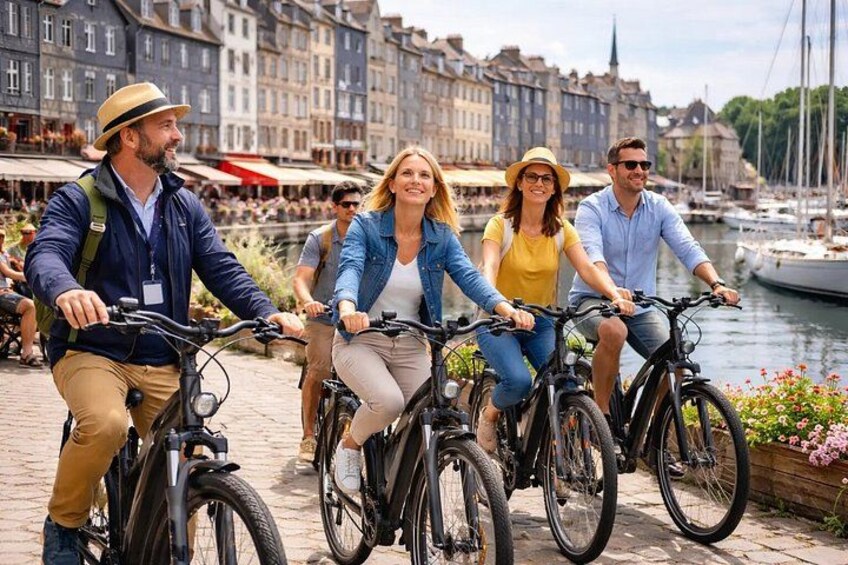 A group of people riding bicycles along a waterfront promenade with buildings and boats in the background. 3