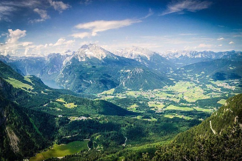 A mountainous landscape with a valley, a lake, and snow-capped peaks. 1