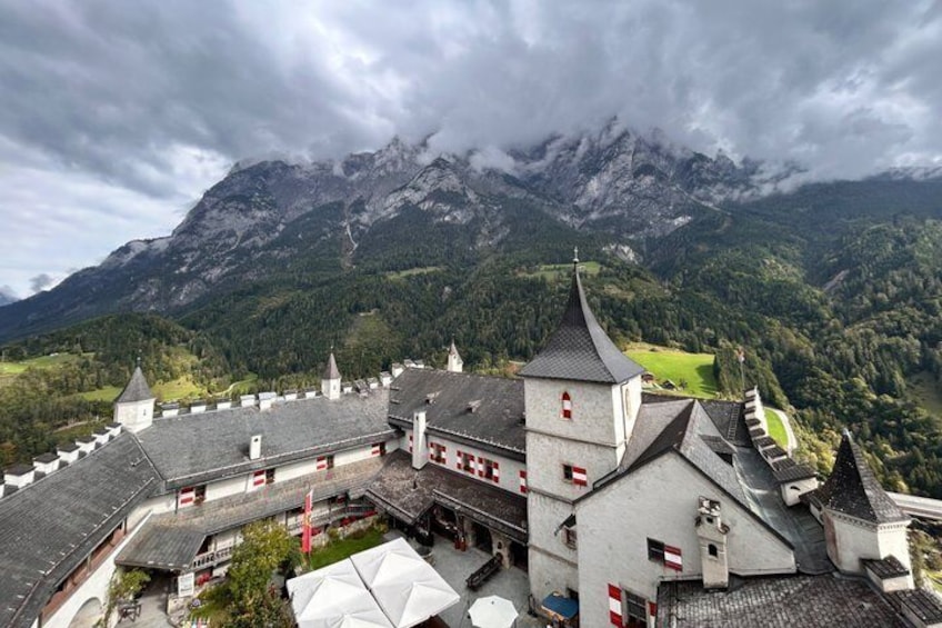 A historic building with a tower, surrounded by lush green mountains and a cloudy sky. 3