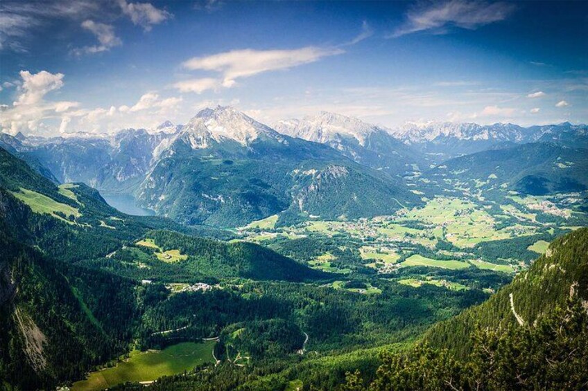 A mountainous landscape with a valley, a lake, and snow-capped peaks. 1
