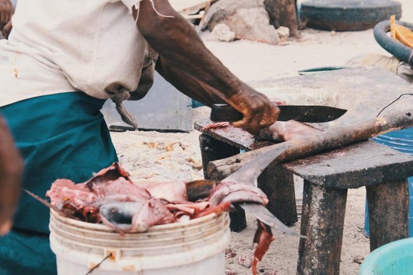 A person preparing fish on a makeshift table, with a bucket of fish and a knife visible. 2