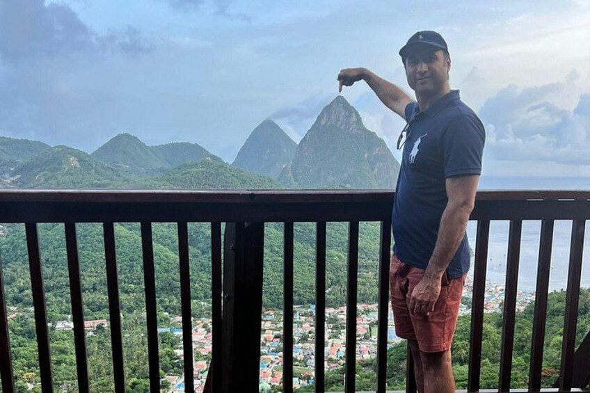 A man standing on a balcony overlooking a mountainous landscape with a town below. 2